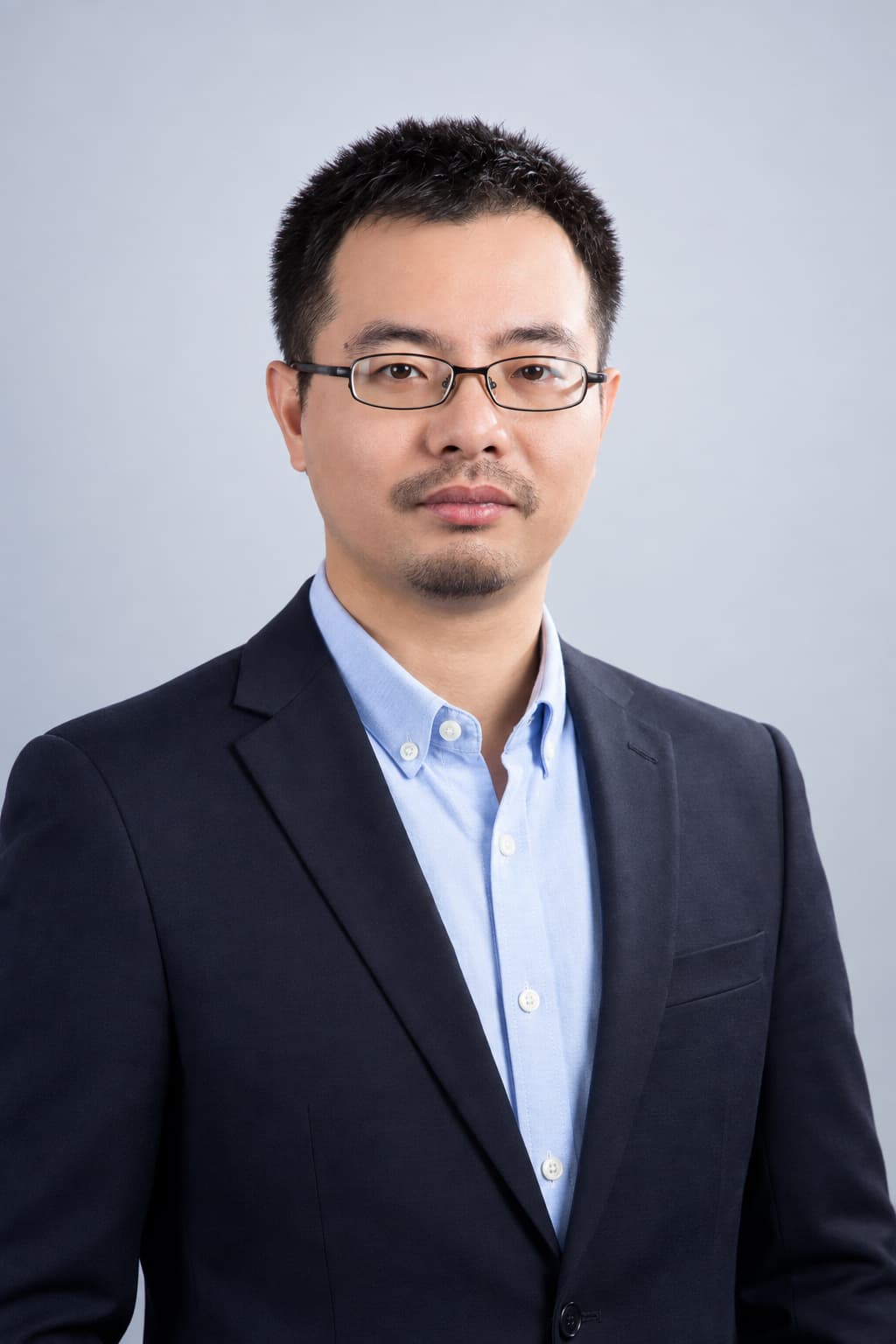 Male colleague in a navy suit, light gray backdrop